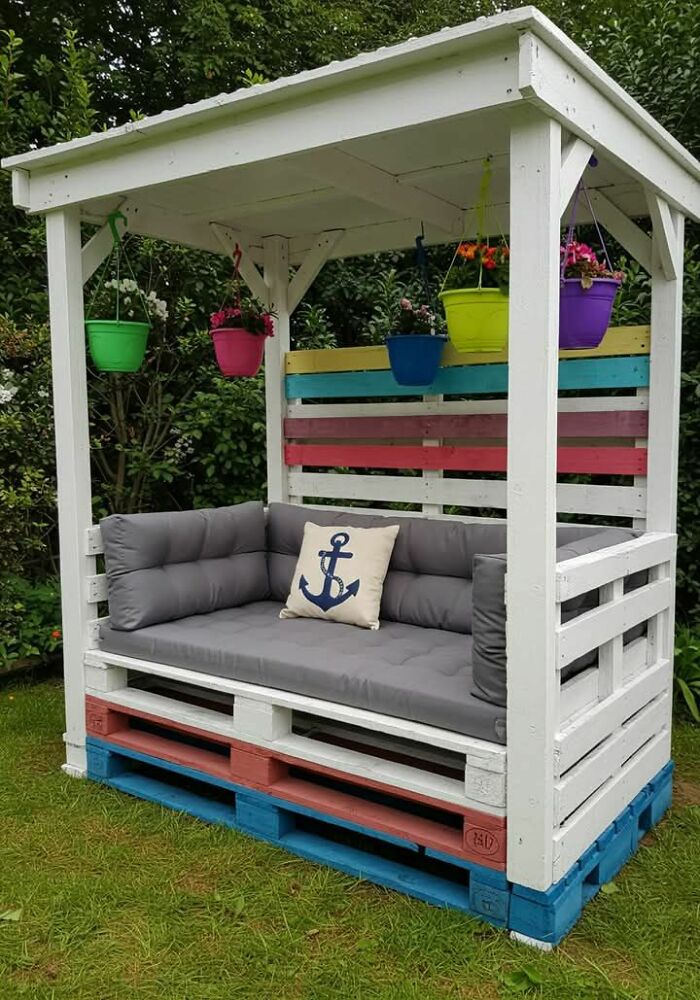 Sofá rústico hecho con madera reciclada y macetas colgantes, demostrando habilidades creativas con la madera.