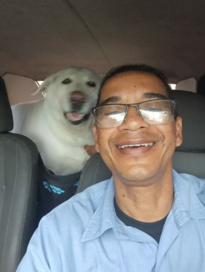 Man smiling in a car selfie with a happy dog, showcasing moments from his pet taxi business.