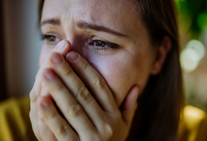 Close-up of a distressed woman covering her mouth, reflecting emotions tied to going home after a prank in a parking garage.