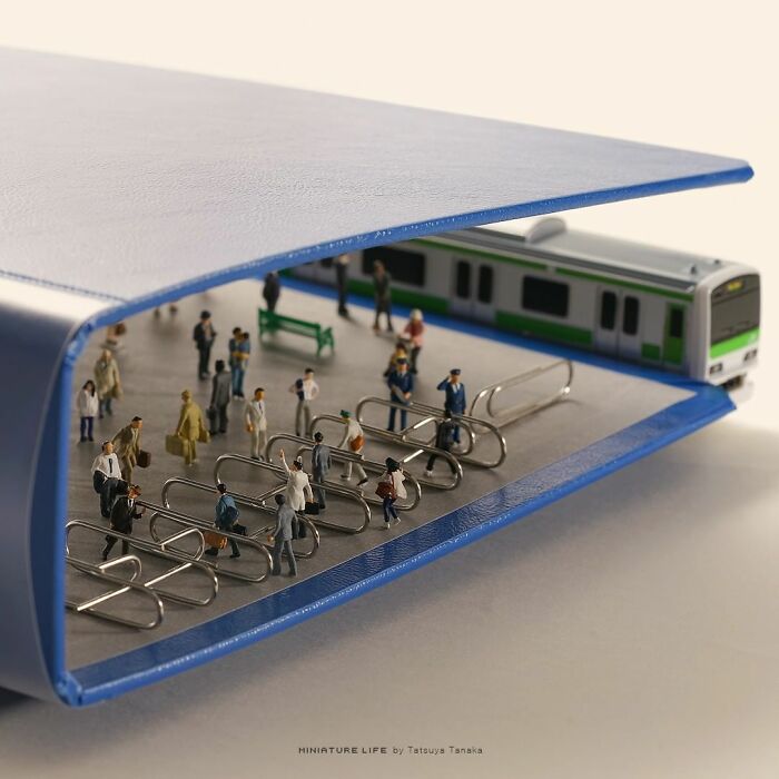 Miniature train station scene inside a blue binder, featuring tiny figures and a train, creating a secret world.