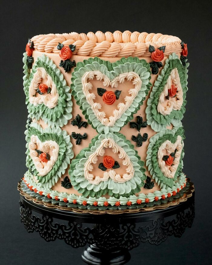 Vegan cake with intricate bug and heart decorations, featuring green and peach icing details on a black stand.