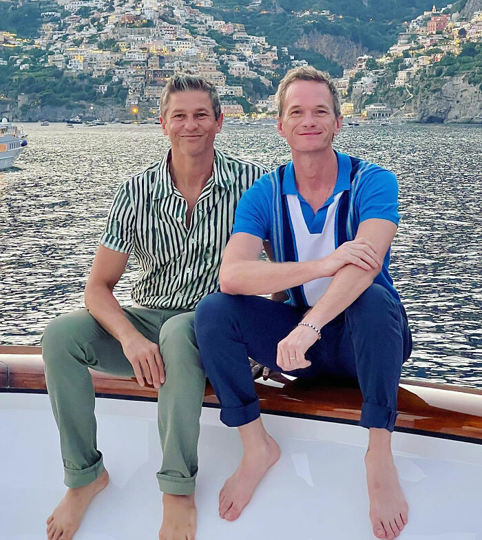 Two men sitting on a boat in front of a scenic coastal backdrop, enjoying a trip.