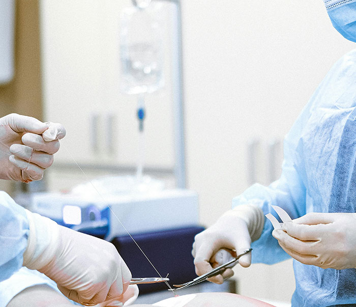 Plastic surgery scene with two professionals in protective gear, focusing on surgical instruments in a clinical setting.