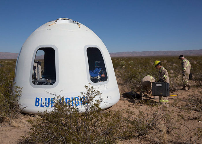 Blue Origin capsule landed in desert with personnel working nearby amidst conspiracy discussions.