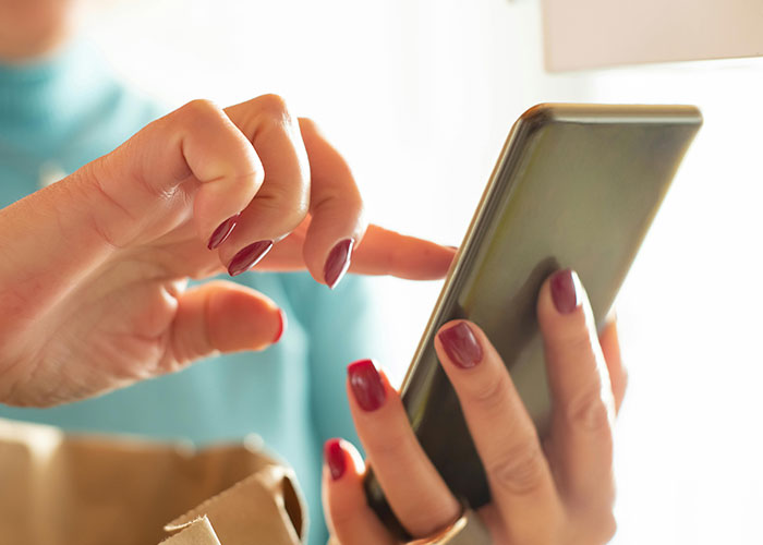 Person using a smartphone on a plane, typing with manicured nails.