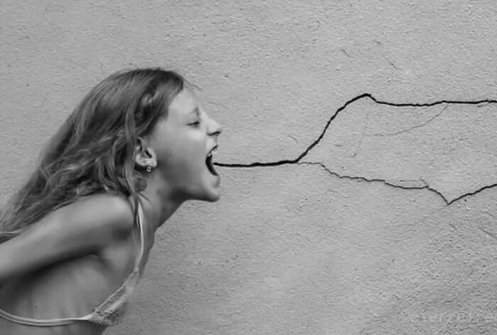 Young woman appearing to shout at a c*****d wall in creative black and white street photography style.