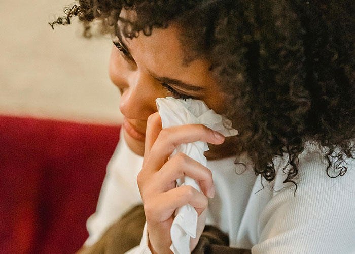 Woman with curly hair wiping tears with tissue, expressing heartbroken emotions related to cheating in a relationship.
