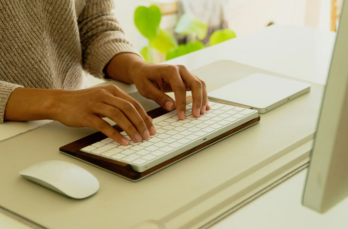 Hands typing on a wireless keyboard at a desk with a mouse and computer, illustrating SEO deliverables in progress.