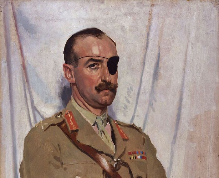 A soldier with an eye patch and mustache in a formal military uniform, posing against a light backdrop.