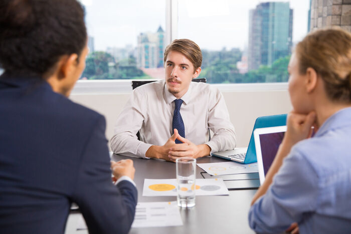 Young man during a job interview, answering questions from interviewers in a modern office setting.