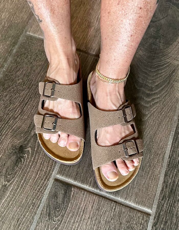 Brown sandals on feet with a gold anklet, tapping into millennial nostalgia on wooden flooring.