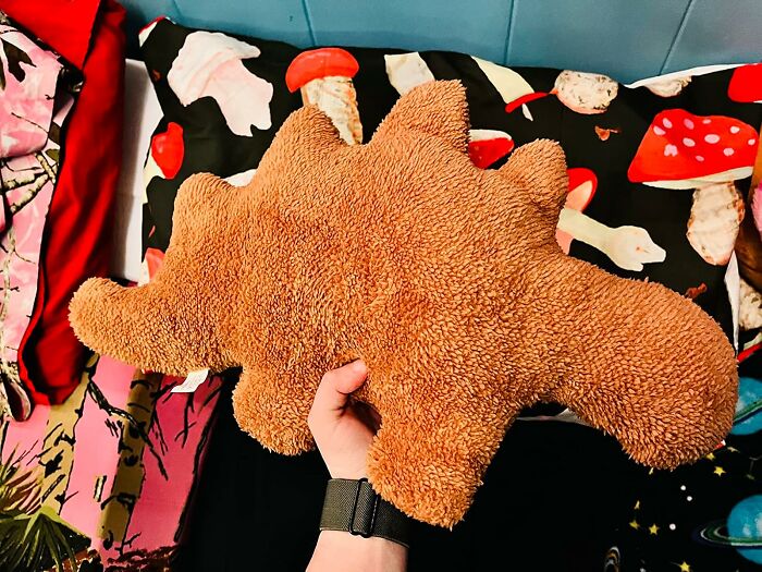 Hand holding a soft plush dinosaur toy, one of the 23 items that will unleash your inner child at any age.