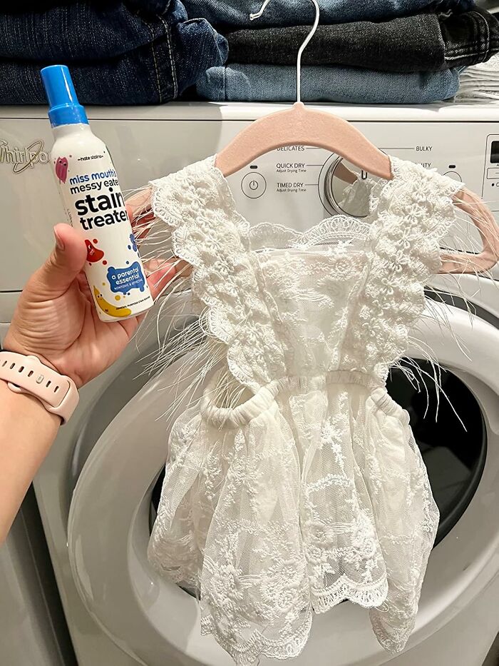 Hand holding stain remover with a lace dress in front of washing machine, suggesting a fresh start with no-stress laundry tips.