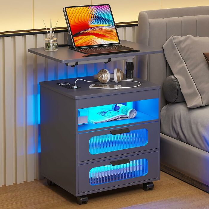 Smart home product: multifunctional side table with LED lighting, headphone stand, and laptop space by a bed.