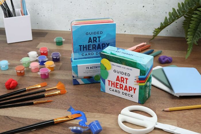 Guided art therapy card decks with painting supplies on wooden table, ideal creative Mother's Day gifts for a thoughtful reaction.