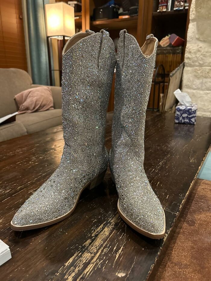 Glittering cowboy boots on a wooden table, perfect for your festival survival kit from Amazon's Festival Shop.