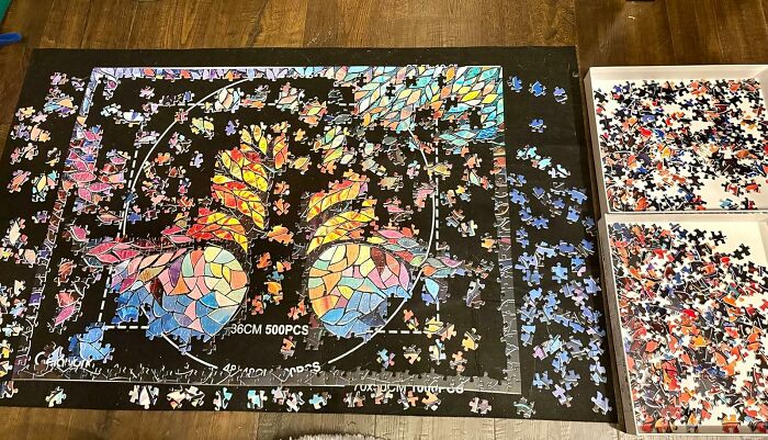 A colorful jigsaw puzzle in progress, featuring vibrant patterns, pieces scattered and sorted in trays on a wooden floor.