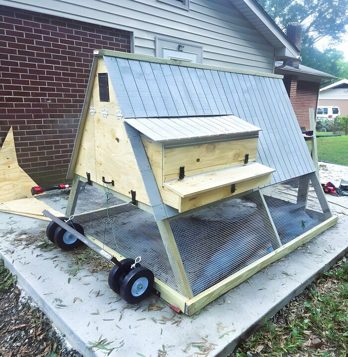 Woodworking ideas shown in a detailed wooden A-frame chicken coop with wire mesh and a metal roof on wheels.
