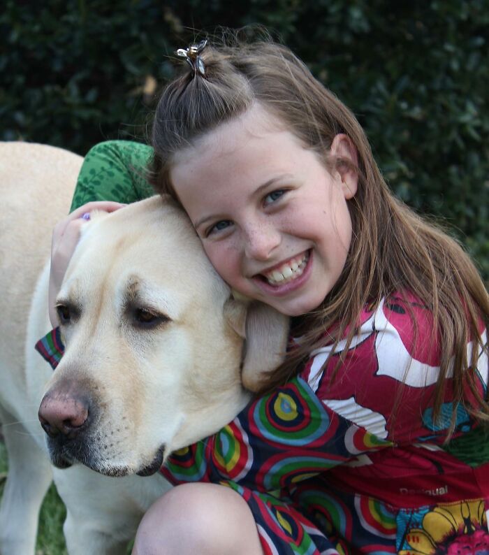 Young girl smiling and hugging Breuer, the Labrador winning Instagram with his late brother&rsquo;s spirit alive outdoors.