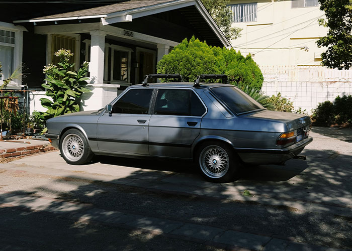 Vintage car parked in driveway of suburban home, with lush green shrubs around, illustrating HOA disputes.