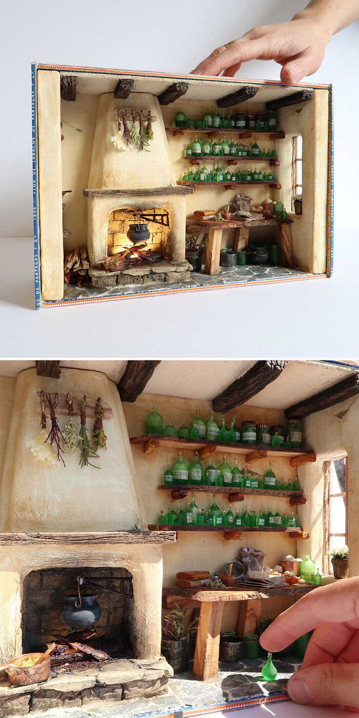 Miniature kitchen scene by Tamar Cohen, featuring a tiny fireplace, wooden shelves, and glass bottles, with a hand for scale.
