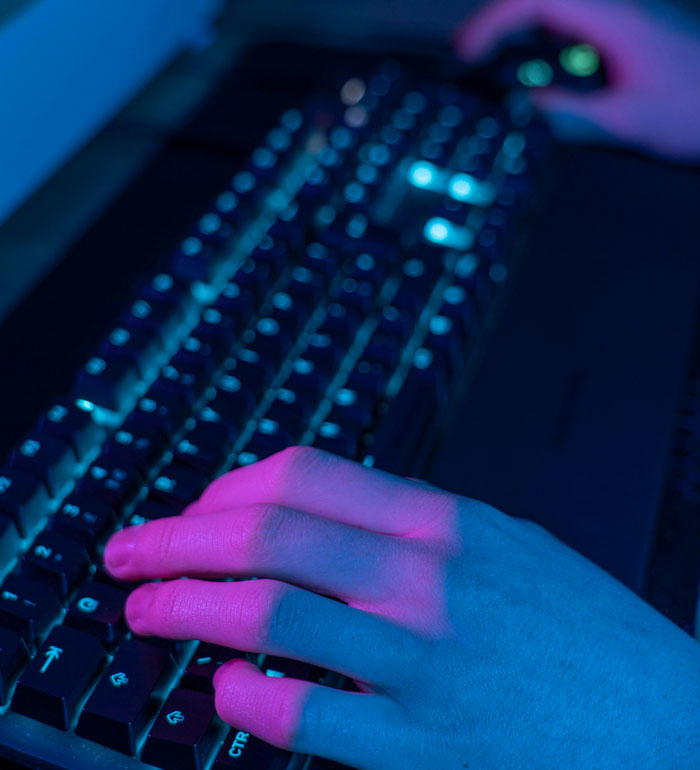 Hands on a keyboard in a dark room, illuminated by pink and blue lights, symbolizing internet hacks.