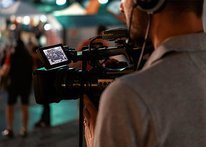 Videographer filming a bustling street event, capturing wild rumors turned true.