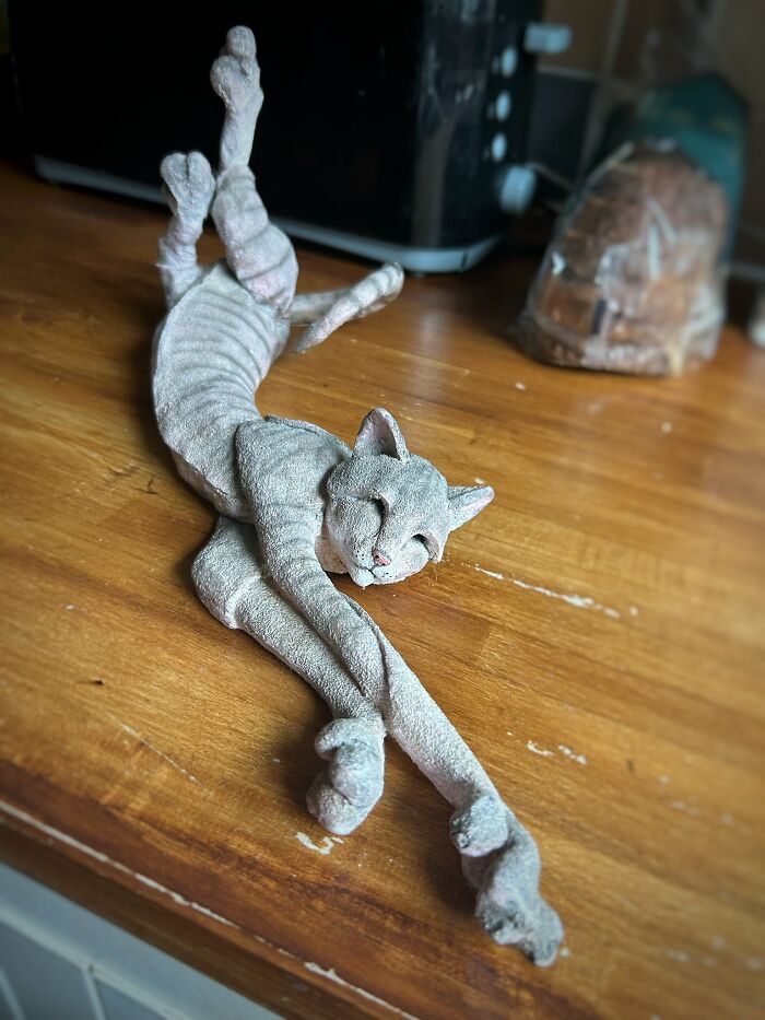 A quirky cat sculpture with elongated limbs found in a secondhand shop, lying on a wooden surface.