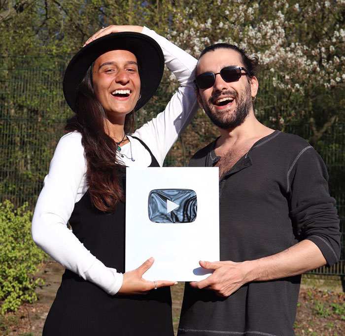 Two smiling people outdoors holding a YouTube award, highlighting a mysterious illness while traveling.