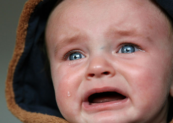 Crying baby close-up, with a tear on cheek, looking distressed on a plane.