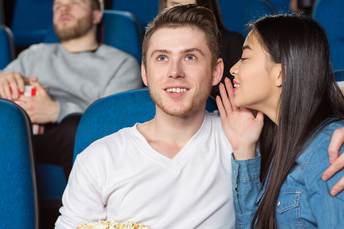 A woman whispering to a man with popcorn in a movie theater, showing a super normal thing in a country setting.