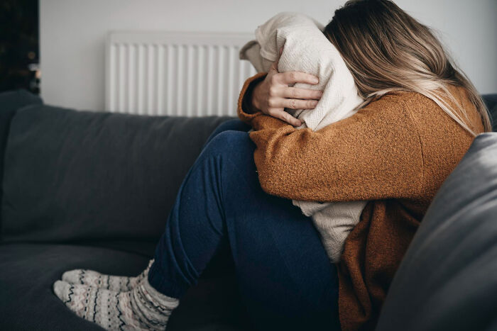 Woman in cozy sweater, hugging a pillow on a sofa, reflecting on relationship insights guys learn about women.