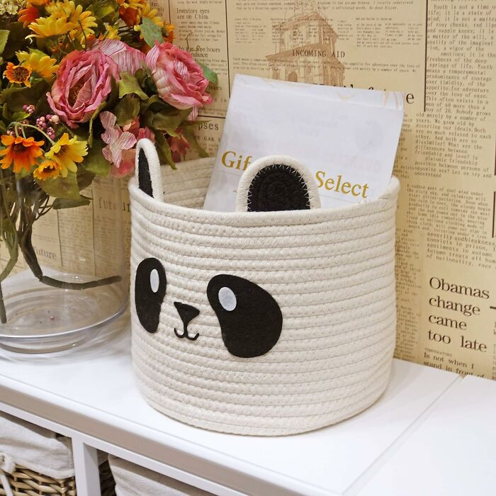 Panda-themed basket with a Bored Panda children's book inside, placed on a shelf beside a vase of flowers.