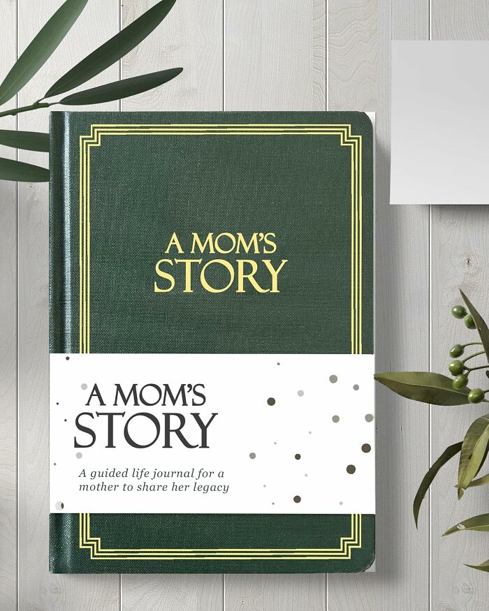 Green hardcover journal titled A Mom's Story, a guided life journal, styled as a unique Mother's Day gift idea on a wooden table.