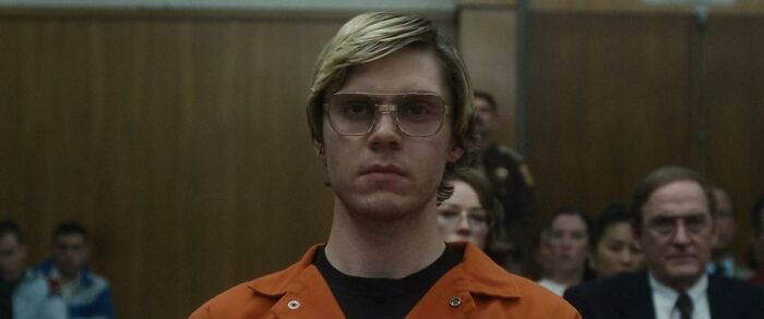 Person in a courtroom, wearing glasses and an orange jumpsuit, surrounded by seated people, representing trusting one's gut.