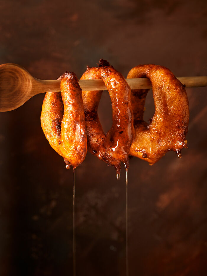 Dripping honey-glazed pastries hanging from a wooden spoon, showcased in the 2025 World Food Photography Awards shortlist.