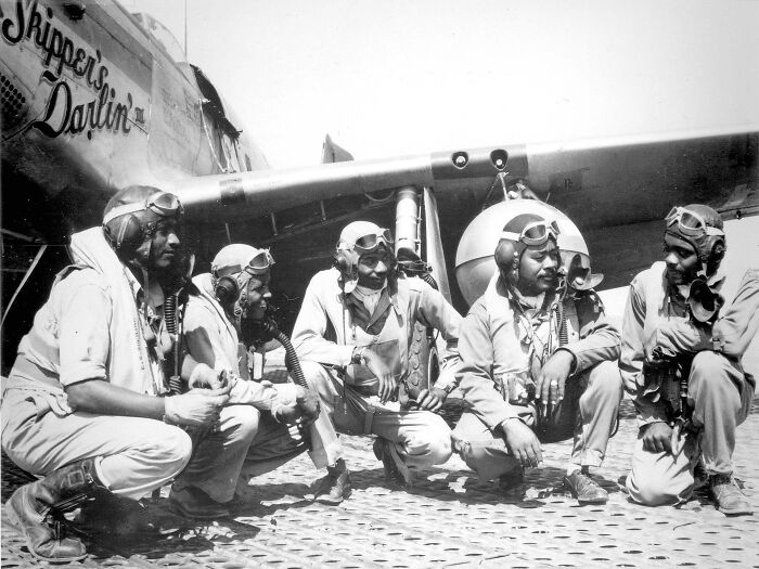 WWII pilots in flight gear gather for a moment of camaraderie beside their aircraft, exemplifying frozen moments in history.