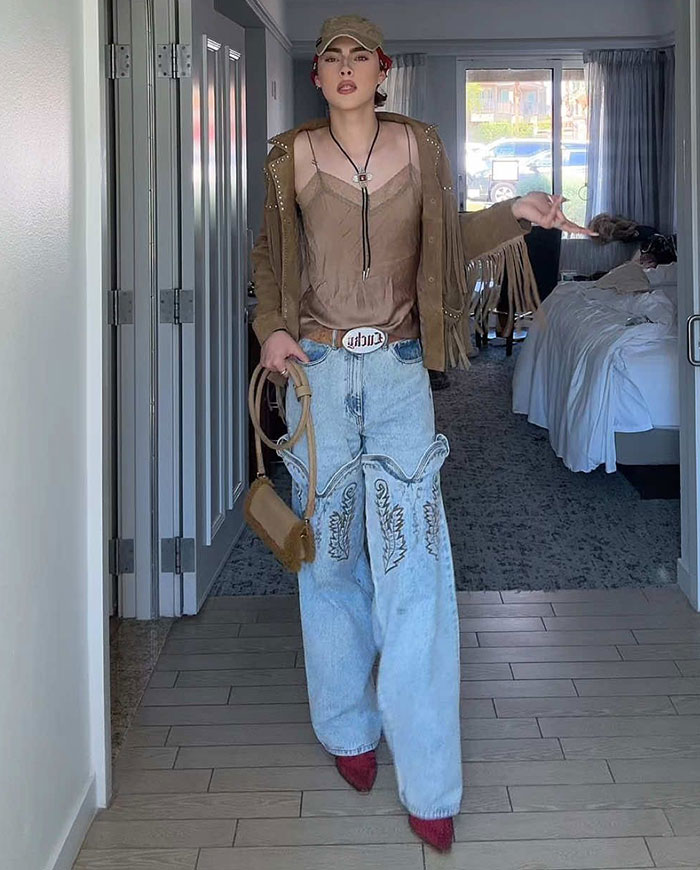 Celebrity in unique outfit at Coachella 2025, featuring oversized jeans and accessories, inside a room.