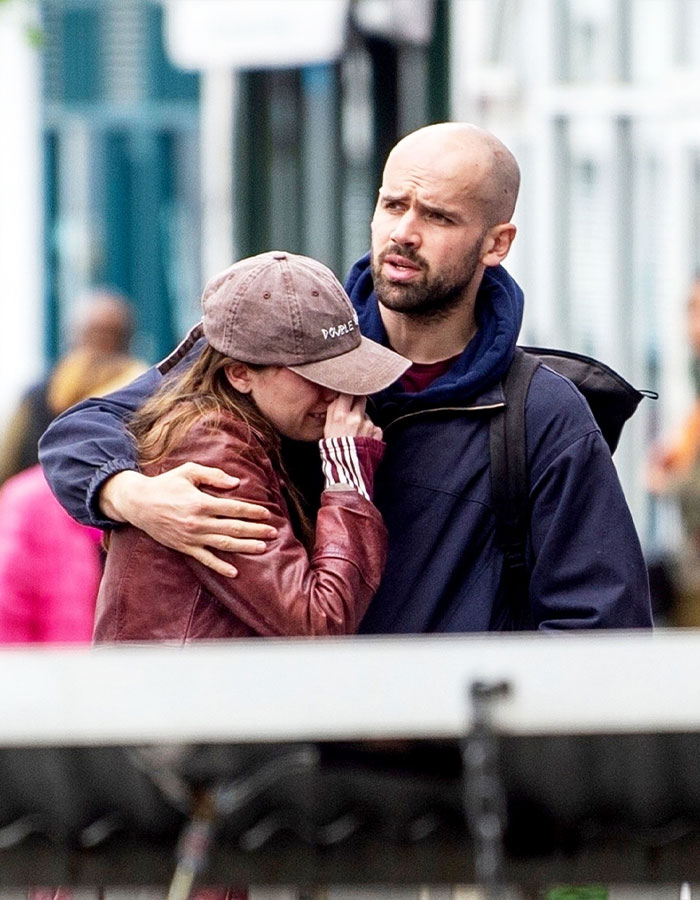 Aimee Lou Wood comforted in public, wearing a cap and jacket, amidst emotional scene.