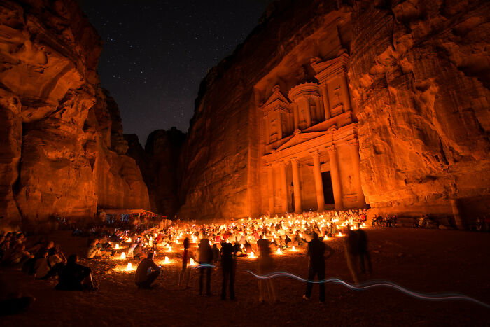 Illuminated underground city site with a crowd gathering at Petra, showcasing ancient architecture amid night sky.