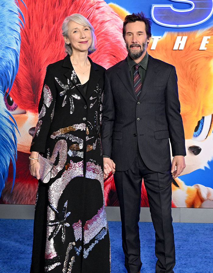 Keanu Reeves in a suit with a woman in a floral dress at a movie premiere event.