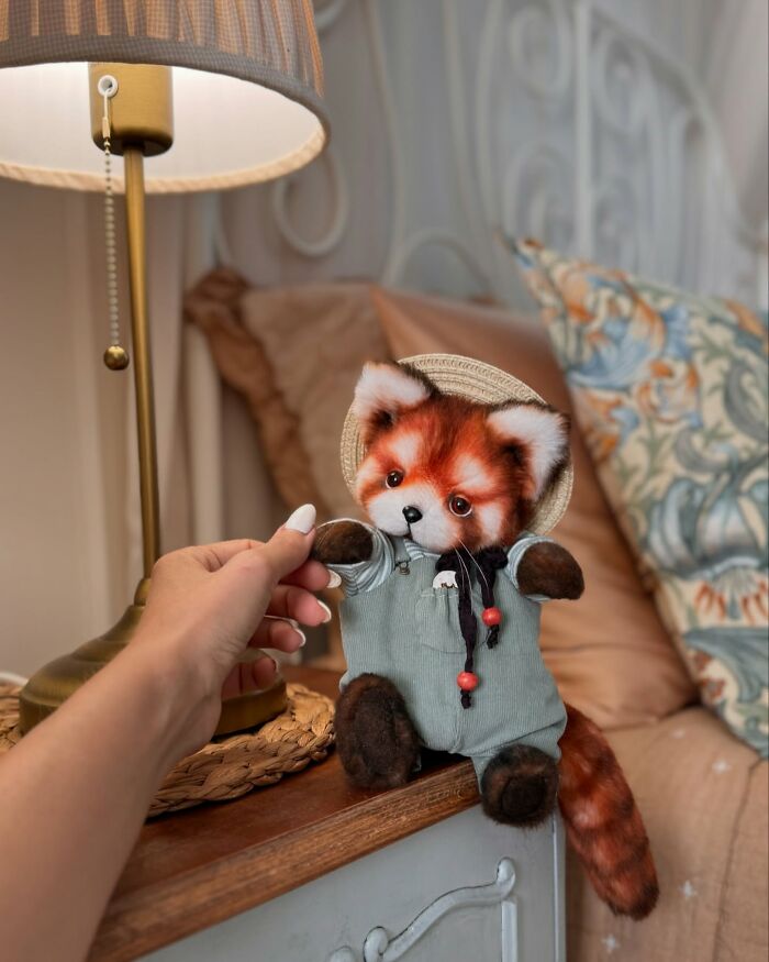 Whimsical plush toy of a fox in a hat and green outfit, posed on a bedside table near a lamp.