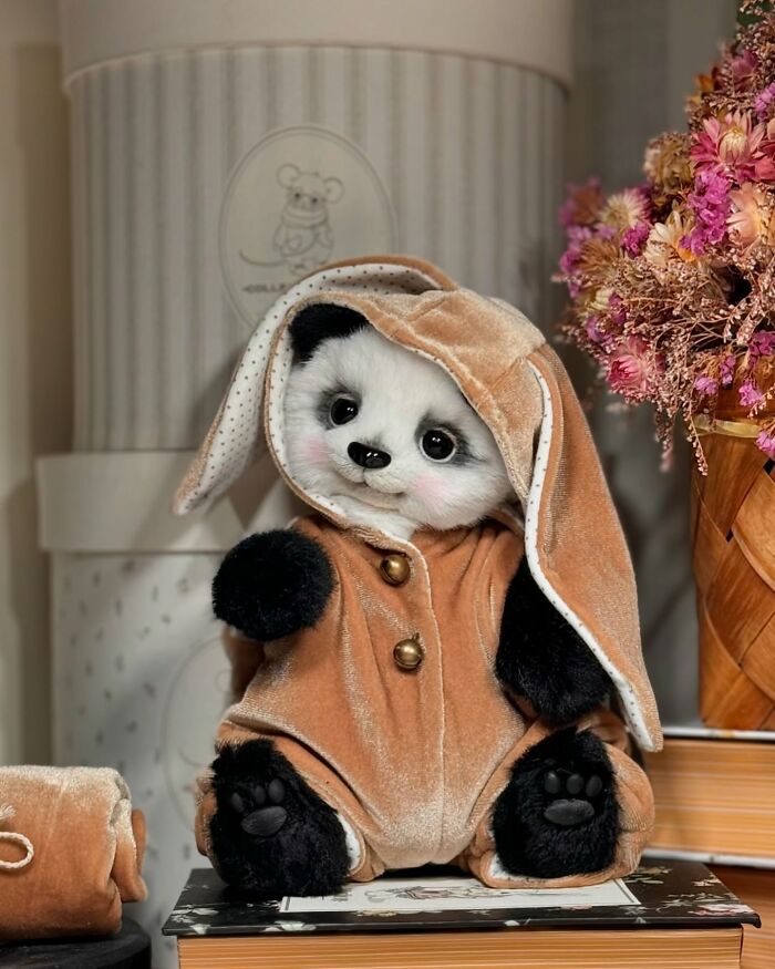Cute handmade whimsical plush toy panda in a soft tan outfit with long ears, sitting beside a basket of flowers.
