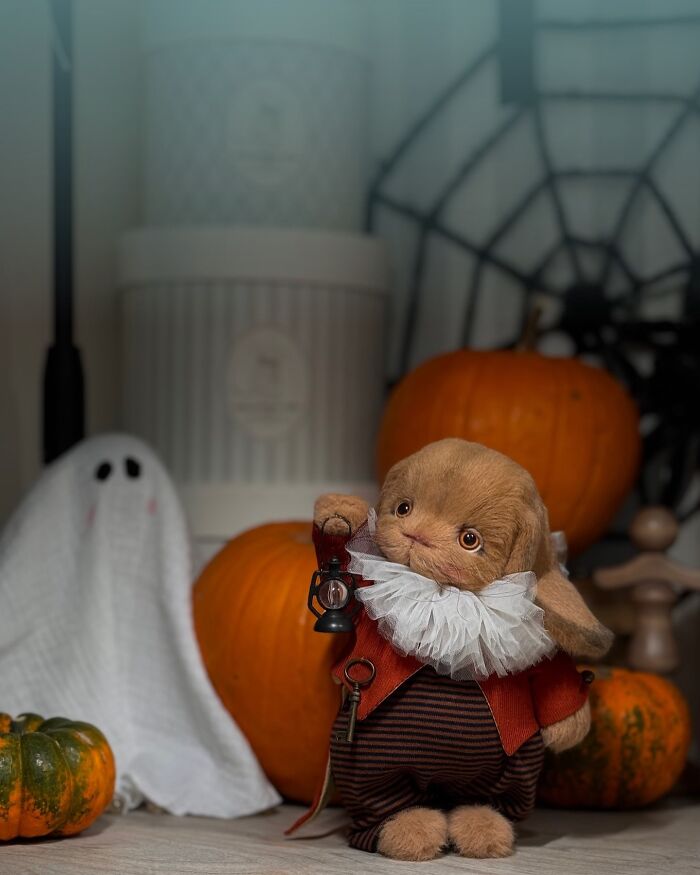 Whimsical handmade plush toy bunny in a festive Halloween setting with pumpkins and a ghost decoration.