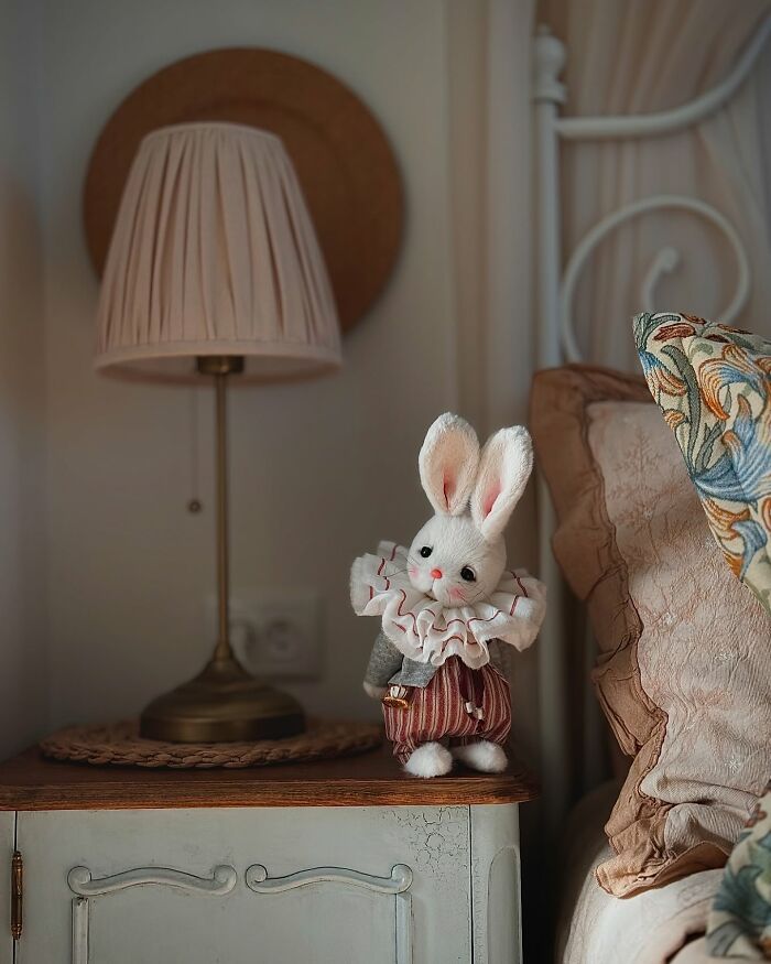 Whimsical plush toy rabbit with ruffled collar on a bedside table near a lamp.