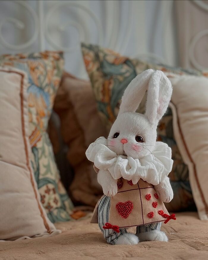 Whimsical handmade plush bunny with ruffled collar and heart-patterned outfit on a decorated bed.