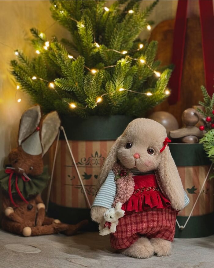 Whimsical handmade plush toy bunny dressed in festive attire, near a decorated tree with lights.