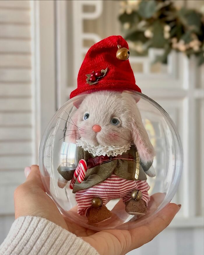 Whimsical handmade plush toy rabbit in festive attire held in a clear sphere.