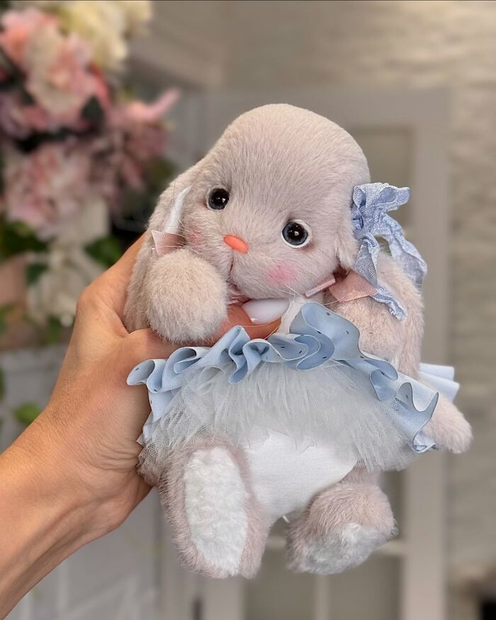 Whimsical plush toy rabbit with a blue ruffled dress, held in hand, featuring handmade details and soft fur.