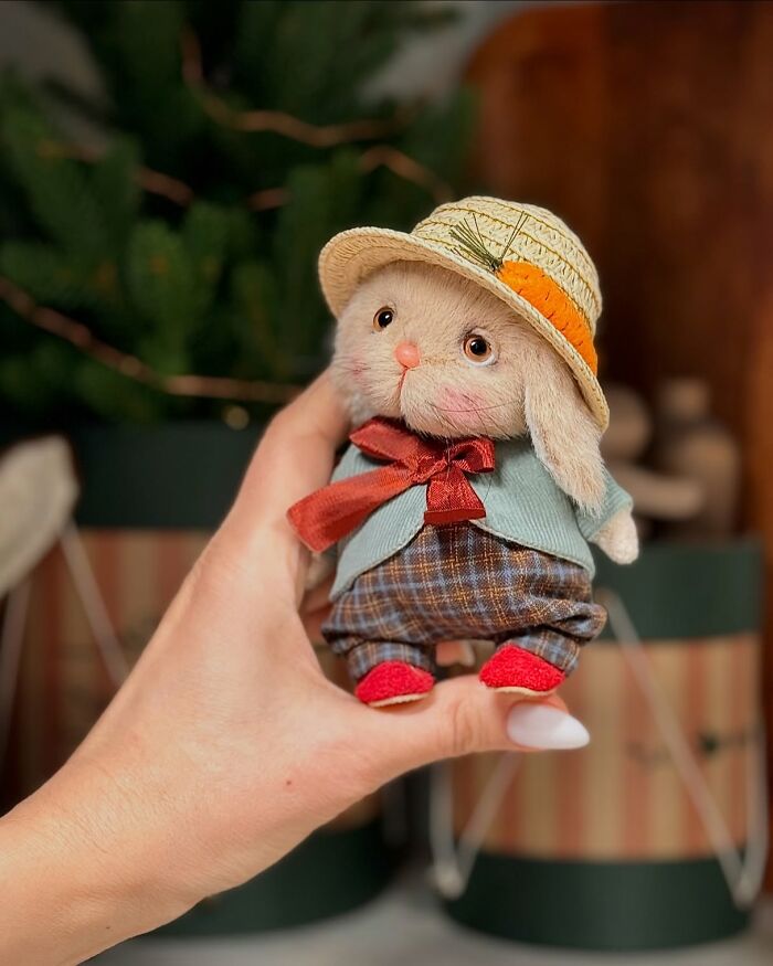 Handmade whimsical plush toy bunny in a hat and scarf, held in a person's hand.